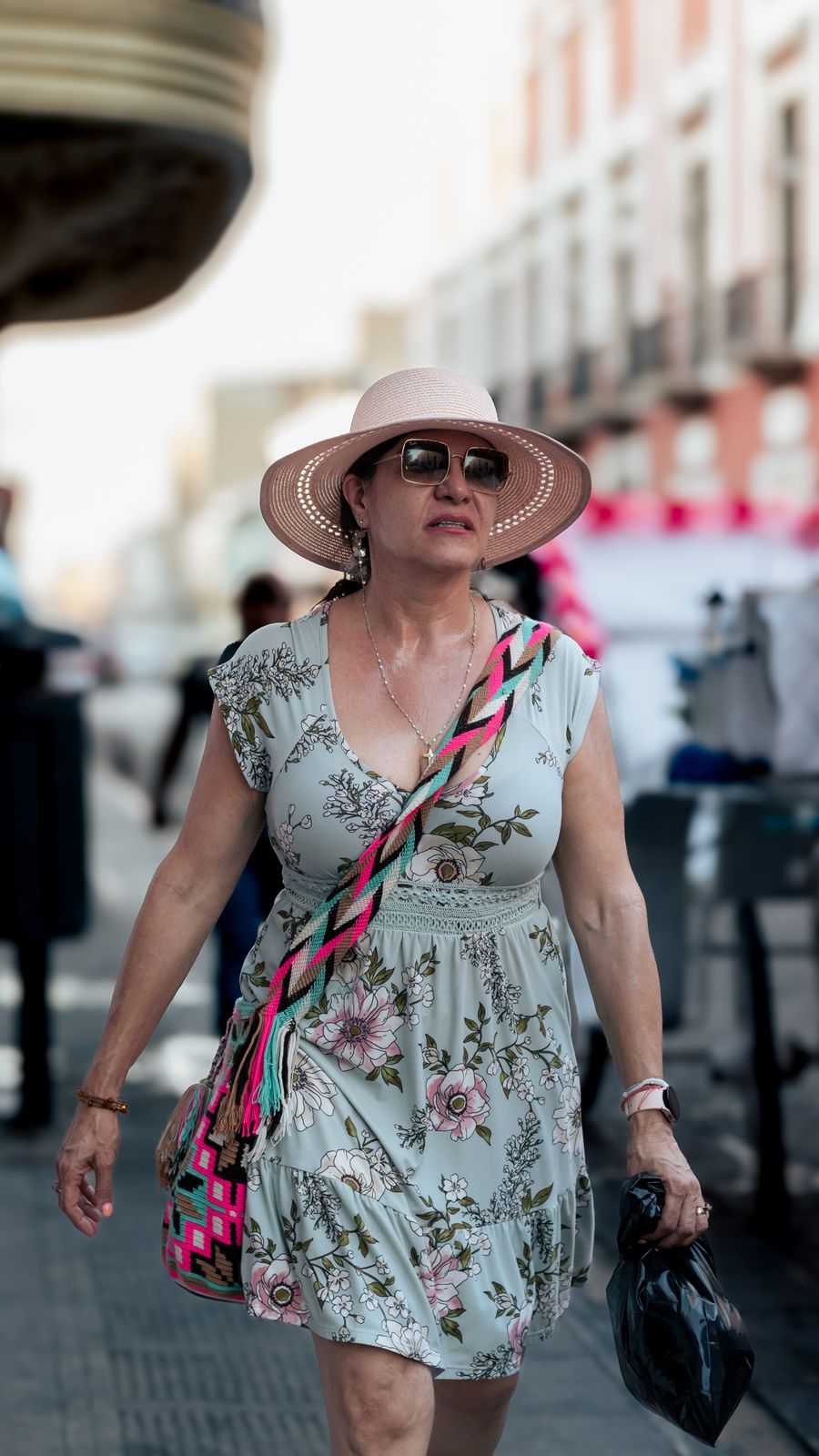 A woman in a floral midi dress and hat walking on a sunny street