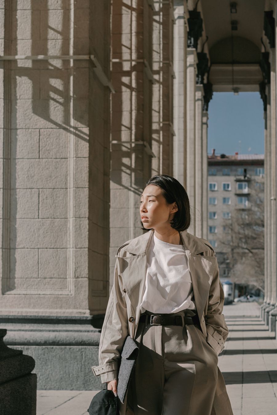 A woman in a trench coat walking through a sunlit corridor