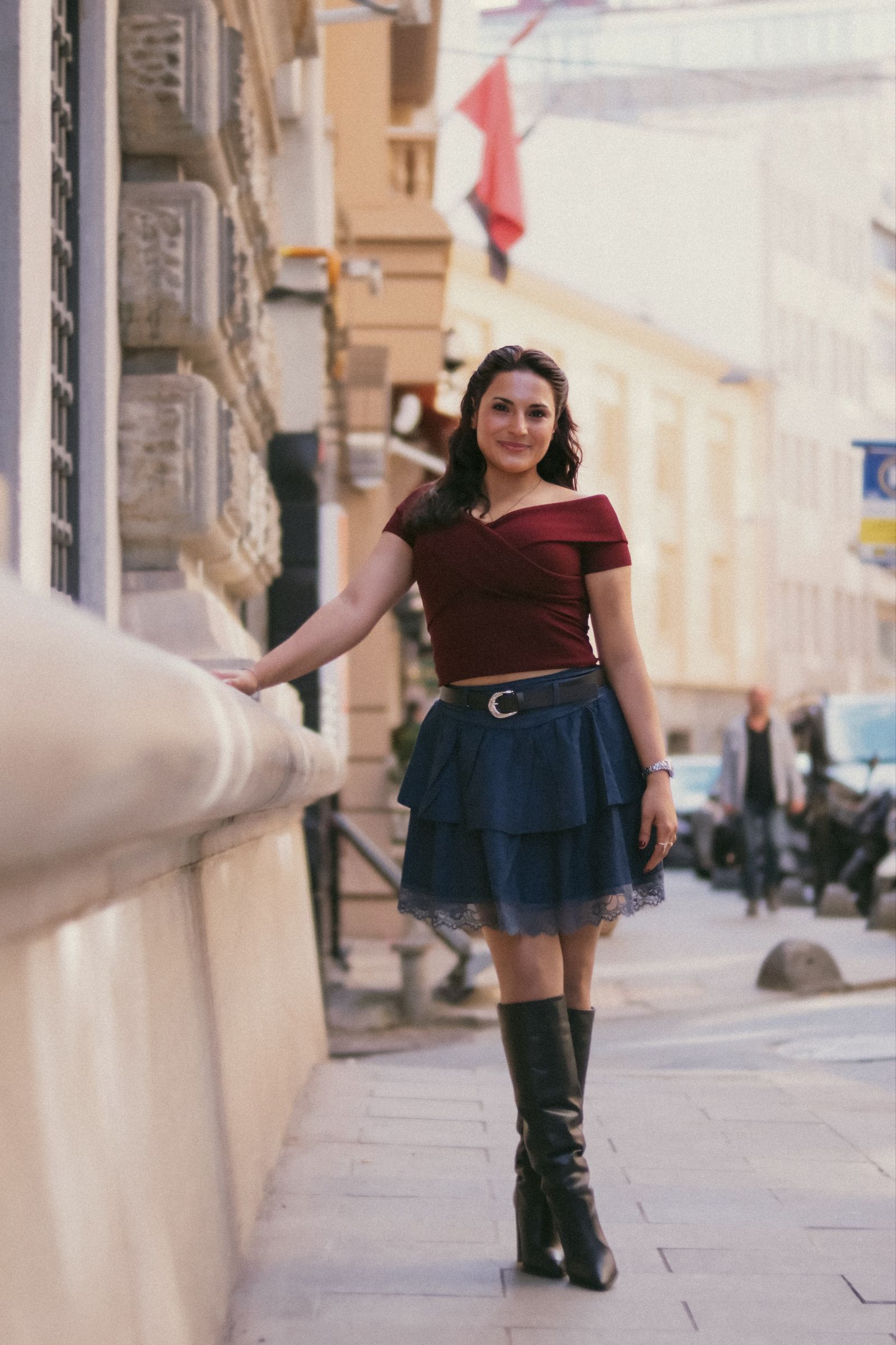 A woman in a coat and midi skirt walking along a sunlit city street