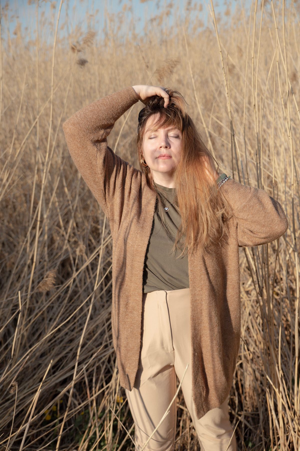 A woman in a long cardigan standing in a sunlit grass field